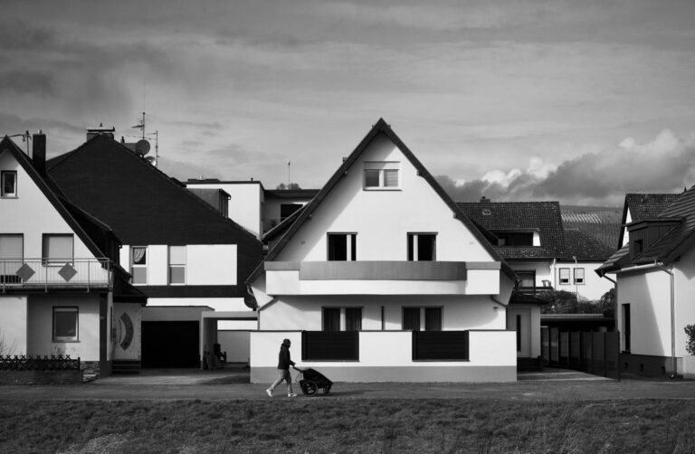 Kinderwagen auf Gehweg mit Eltern und Garten mit smartem Mähroboter im Hintergrund